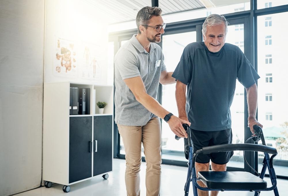 Physical therapist assisting an older ALS patient using a walker to support mobility during symptom progression